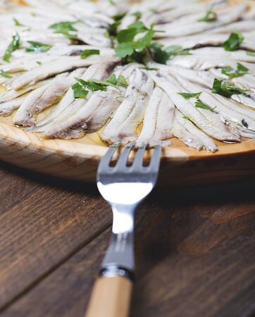 Close-up of anchovies with olive oil and vinegar on a wooden plate next to a fork on a brown wooden table. Healthy food.の写真素材