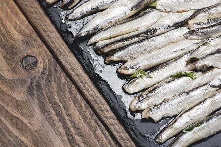 Anchovies with olive oil and vinegar on a plate of slate on wooden table. Food.の写真素材
