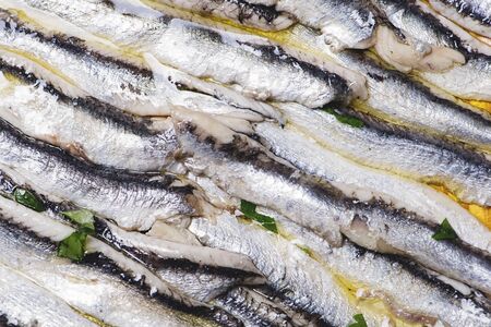Close-up of delicious marinated anchovies with olive oil and vinegar on brown wooden table....