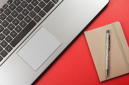 Notebook and pen next to laptop.の写真素材