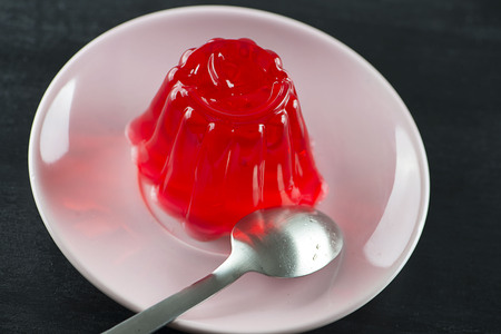 Strawberry jelly on a plate next to a spoon.の写真素材