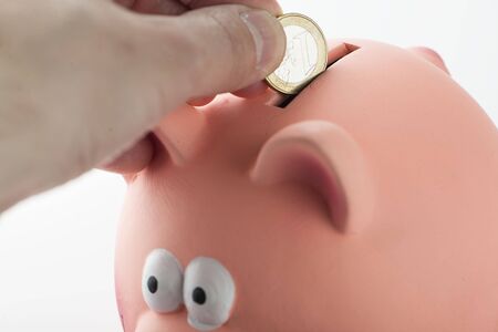 Male hand inserting a coin into a piggy bank.の写真素材