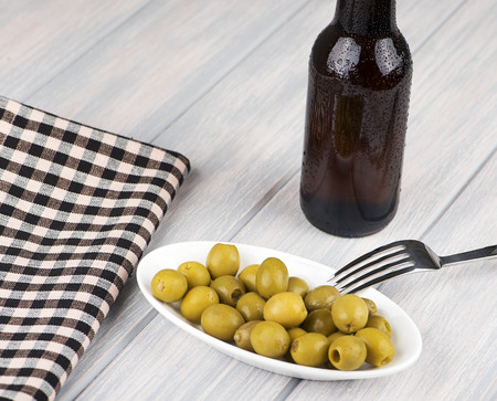 Bottle of beer and olives next to a napkin on wooden table. Alcohol.の写真素材