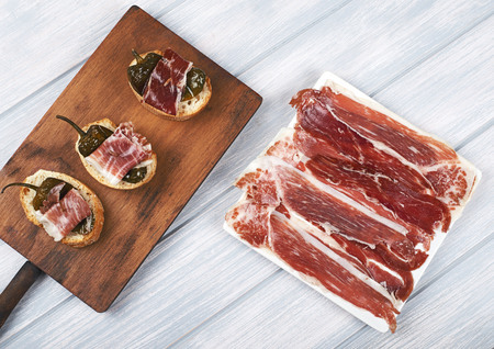 Top view of Spanish tapas of ham and green pepper, and a plate of Iberian ham on white wooden board. Spanish gastronomy.の写真素材