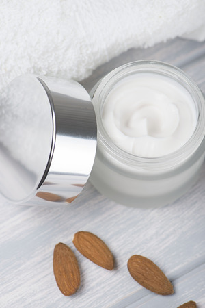 Close-up of a pot of cream for the skin, towel and almonds on white wooden table. Vertical shoot.の写真素材