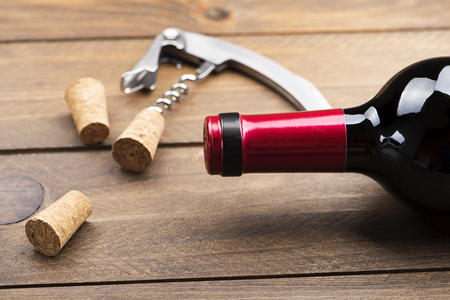 Corkscrew next to several corks and a bottle of wine on wooden table. Horizontal studio shot.の写真素材
