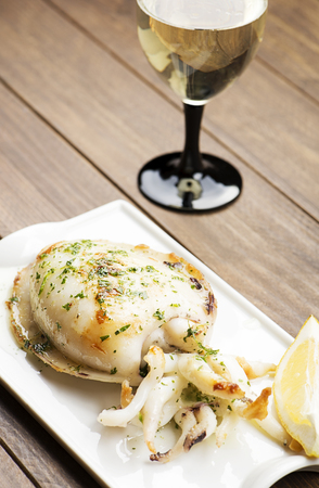 Close-up of cuttlefish with garlic and parsley and lemon next to glass of white wine on wooden...