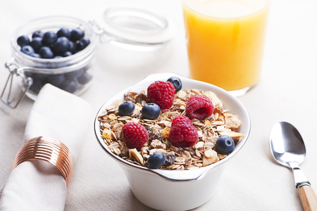 Breakfast cereal with raspberries and blueberries next to orange juice.の写真素材