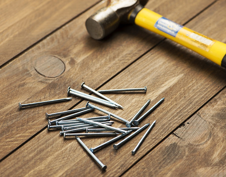 Stacked nails next to a hammer on brown wooden table.  Construction tools