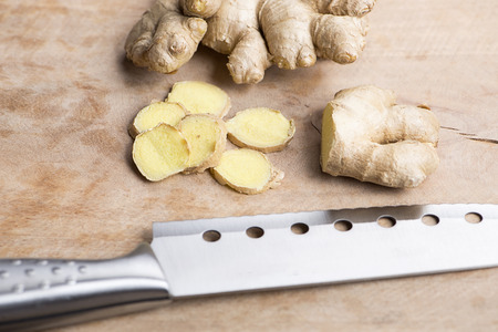 Ginger next to kitchen knife on wood. Food