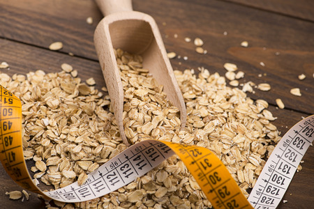 Oatmeal next to wooden spoon measuring tape on wooden table. Diet.の写真素材