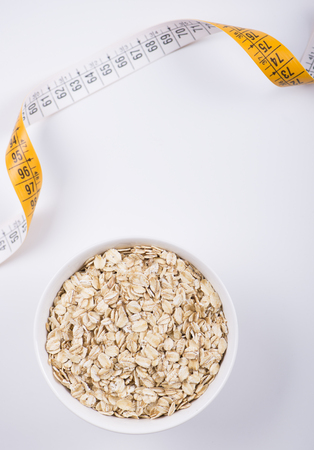 White bowl with oats together yellow measuring tape on white background. Isolated. Diet.の写真素材