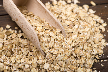 Oats next to wooden spoon on wooden table. Closeup.