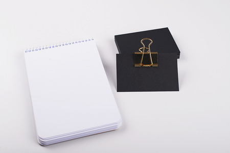 Black cards with golden clip next to notepad on white background. Isolated. Mockup.