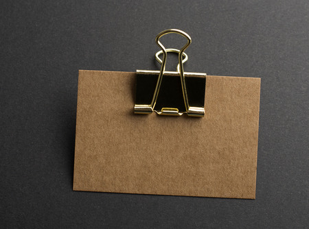 Brown business card with golden clothespin on black background. Mockup.の写真素材