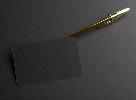 Black business card next to golden pen on black background. Mockup.