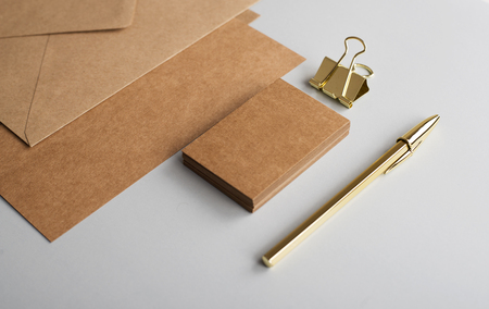 Top view of cards, envelope, business card in brown color with clip and golden ball pen on gray background. Mockup.の写真素材