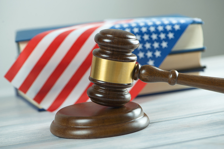 Wooden mallet used by a judge or at an auction next to the US flag and a book. Conceptの写真素材