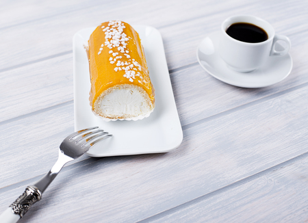 Cream pie and caramel on tray next to coffee, fork and napkin on wooden table. Food