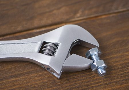 Close-up of spanner next to nut on wooden table. Industry.