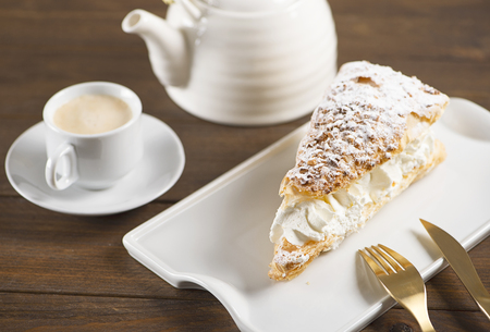 Close-up of delicious breakfast of coffee with sweet puff pastry with cream on brown wooden table....