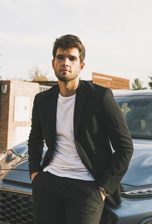 Close-up of attractive young man with beard in suit leaning on his car looks at the camera.suitの写真素材