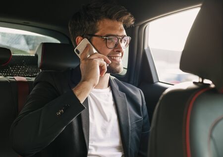 Young and attractive man with a beard and glasses speaks with his smartphone smiling inside a car. Businessの写真素材