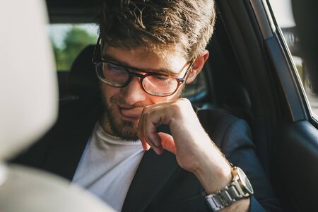 Attractive young man with a beard and glasses with a serious face reads documents inside a car. Businessman.の写真素材
