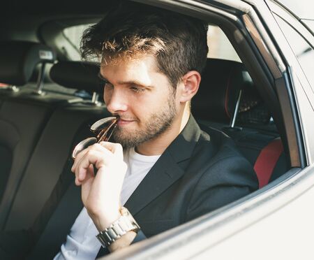 Attractive young man with a beard wearing glasses resting on his mouth is thoughtful inside a car. Businessman.の写真素材