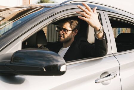 Attractive young man with a beard and glasses gets angry driving his car.の写真素材