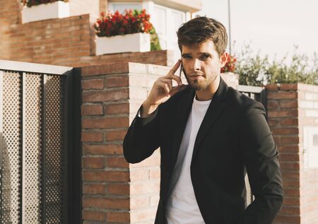 Attractive young man dressed in a beard speaks on the phone and looks at camera.の写真素材