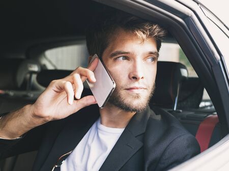 Young and attractive man with a beard speaks with his smartphone in a vehicle that does not drive and looks out the window. Businessの写真素材
