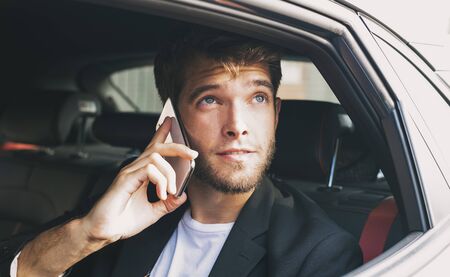 Young and attractive man with a beard speaks with his smartphone in a vehicle that does not drive and looks out the window. Businessの写真素材