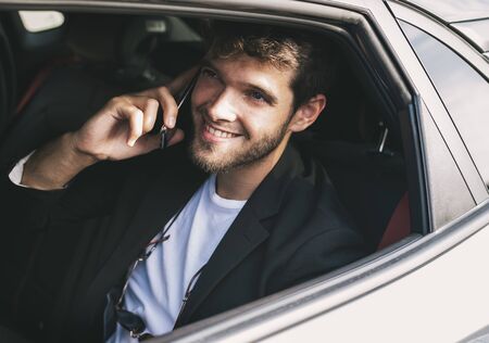 Young and attractive man with a beard smiles and talks with his smartphone in a vehicle he does not drive. Businessの写真素材
