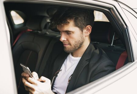Young and attractive man uses his smartphone in a vehicle he does not drive. Businessfix spellingの写真素材