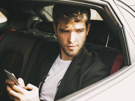 Young and attractive man with a beard and with a smartphone in his hands looks out the window. Businessの写真素材