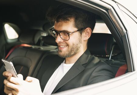 Young and attractive man with a beard and glasses smiles while using a smartphone. Businessの写真素材