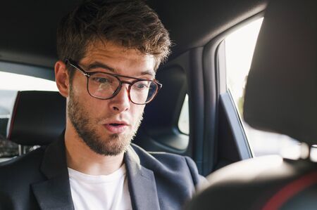 Young and attractive man with a beard and glasses with a surprised face is inside a car. Businessの写真素材