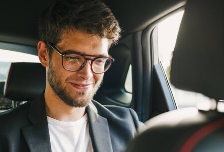 Young and attractive man with a beard and glasses smiles inside a car. Businessの写真素材