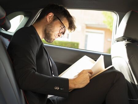 Young and attractive man with a beard and glasses works reading papers inside a car. Businessの写真素材