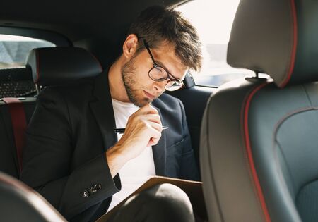 Young and attractive man with a beard and glasses works reading papers inside a car. Businessの写真素材