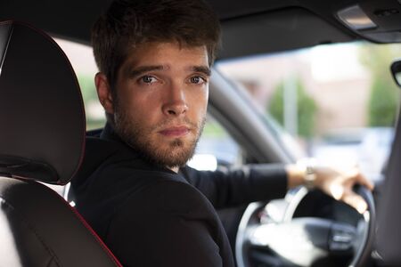 Attractive young man with a beard looks at camera in his car.の写真素材