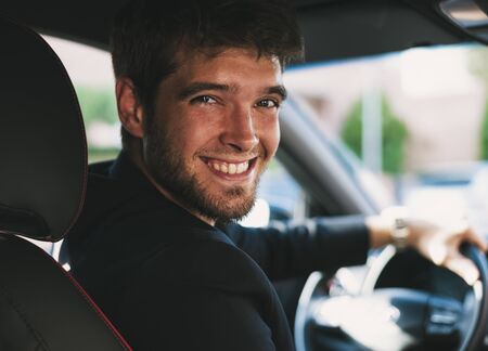 Attractive young man with a beard smiles and looks at camera in his car.の写真素材