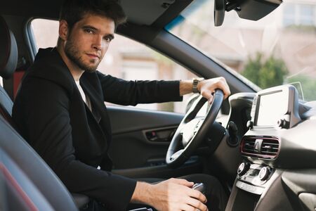 Attractive young man with a beard looks seriously at camera inside his car. Drive.の写真素材