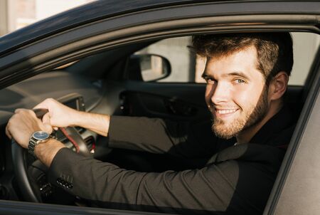 Attractive young man with a beard smiles and looks at camera sitting in his car.の写真素材