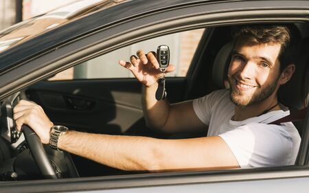 Attractive young man with a beard teaches the camera the keys of his new car.の写真素材