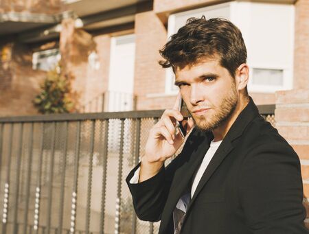 Close-up of attractive young man with beard in suit speaks on the phone looking at cameraの写真素材