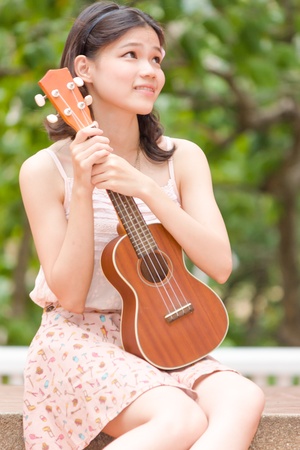Asian girl with ykulele guitar outdoor in happy conceptの写真素材