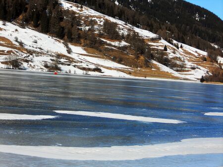 frozen lake in winter with blue sky and snow-capped mountains, Reschenseeの写真素材
