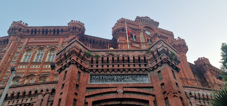 A striking red brick building with an ornate and imposing facade is shown from a low angle. The...